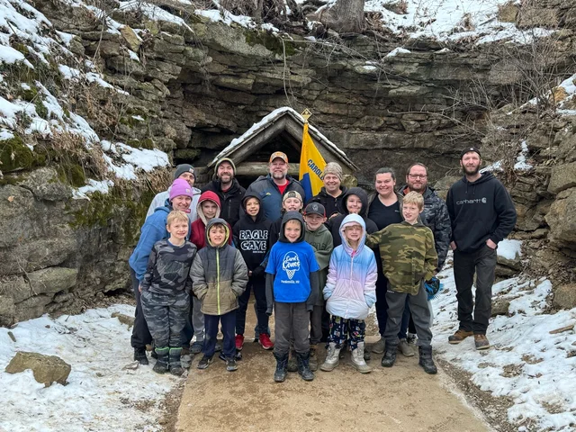 Pack 321 Scouts and families gathered with their Pack flag at the snowy Eagle Cave entrance