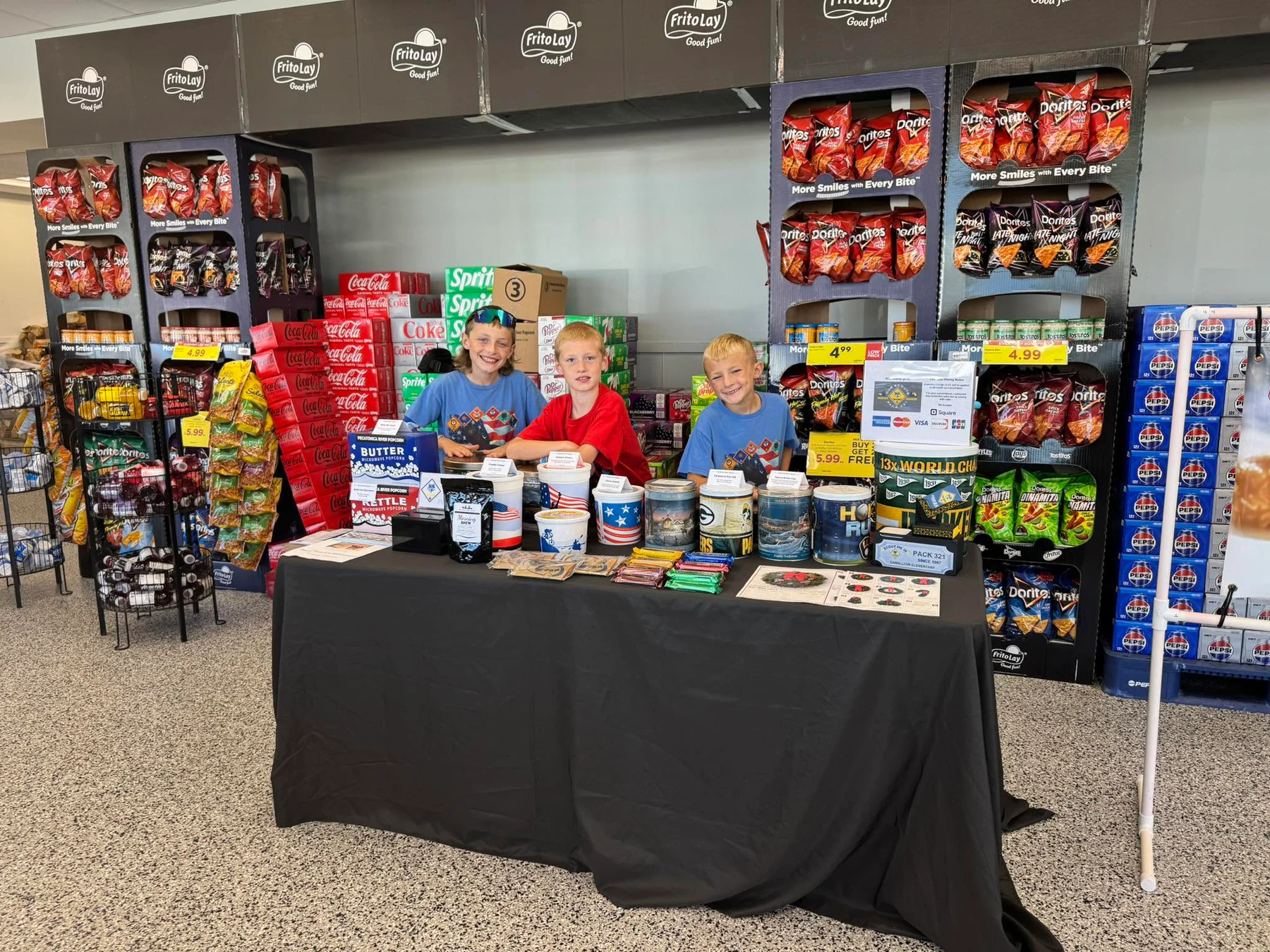 Three Pack 321 Scouts participating in a popcorn fundraiser behind their product table